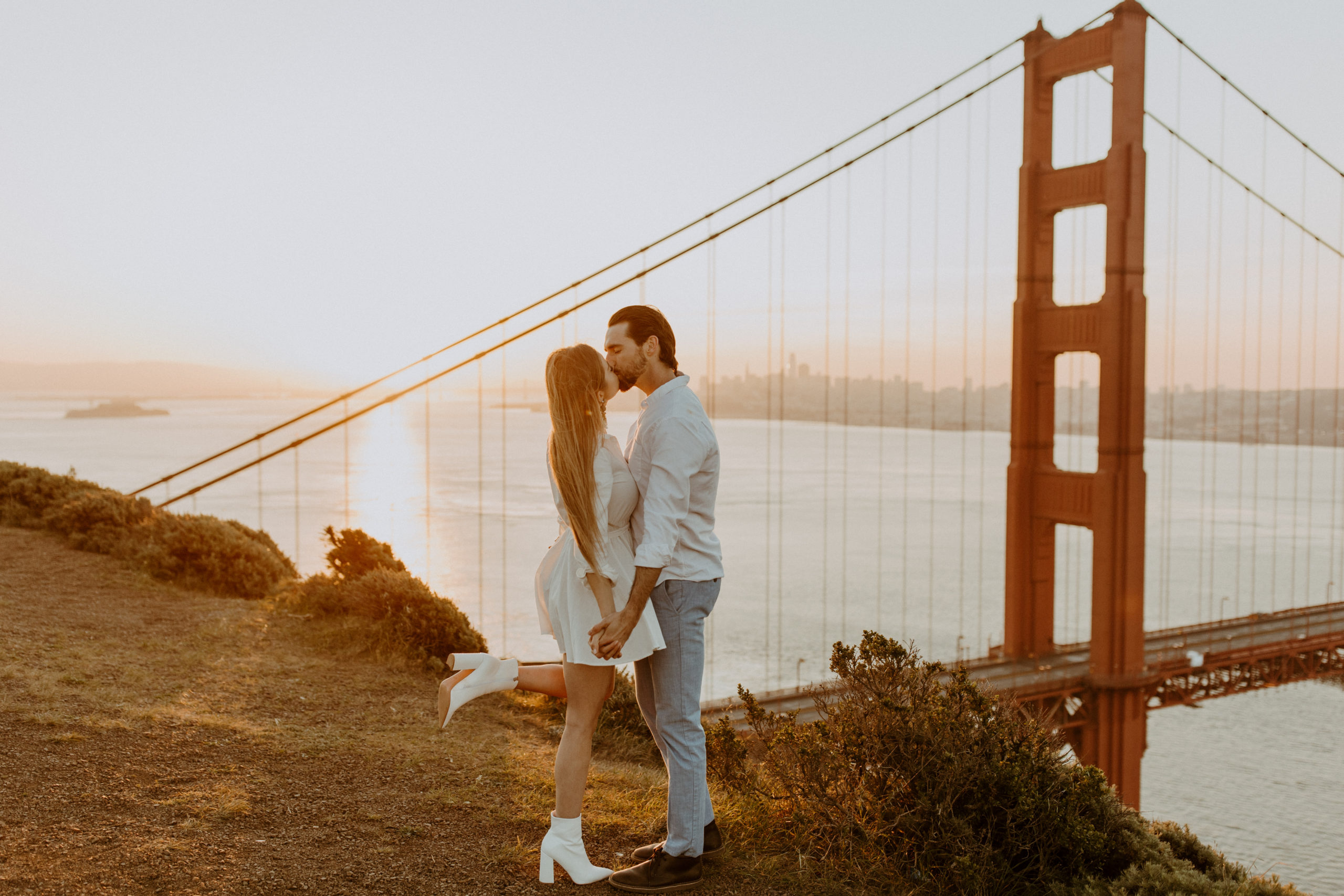 the fiance lifting up her leg behind her as she kisses her fiance at the Golden Gate Bridge in San Francisco