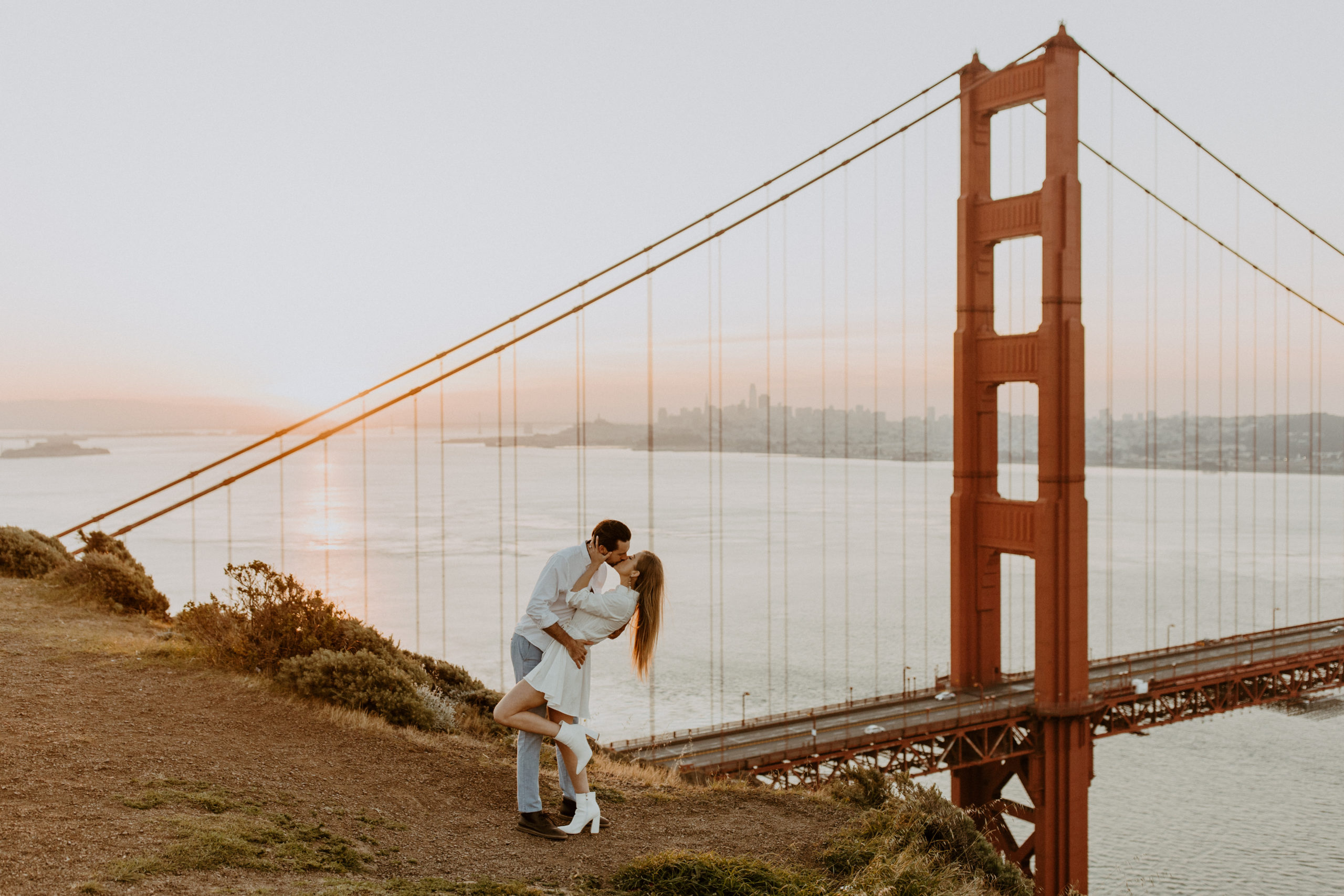 the couple hugging and kissing during the sunrise over the bridge