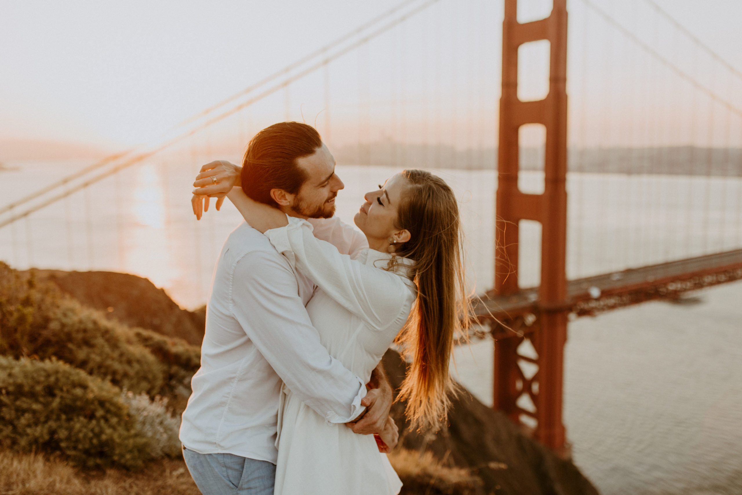 the couple wrapping their arms around each other at the Golden Gate Bridge in San Francisco
