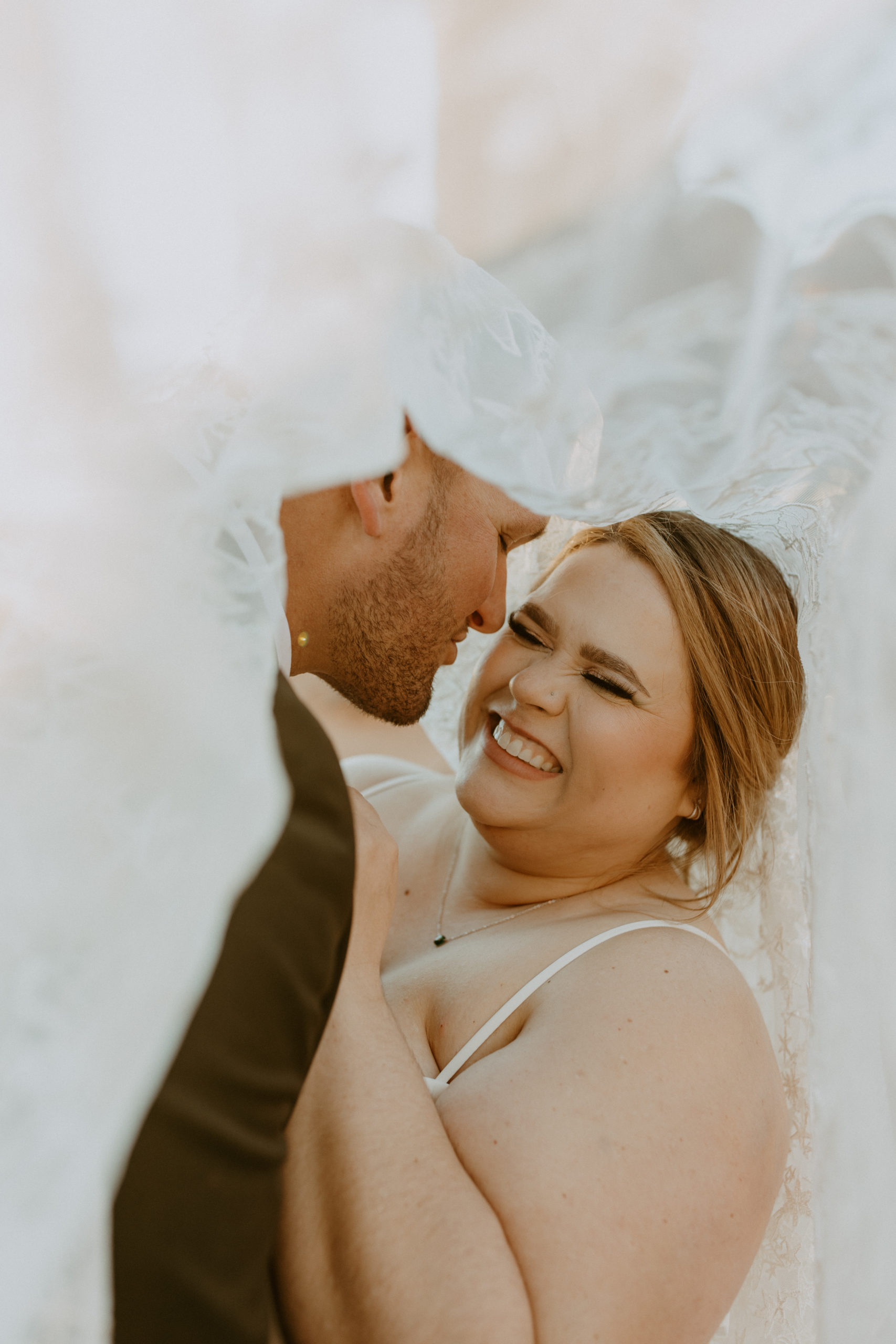 the bride laughing with her husband under the veil