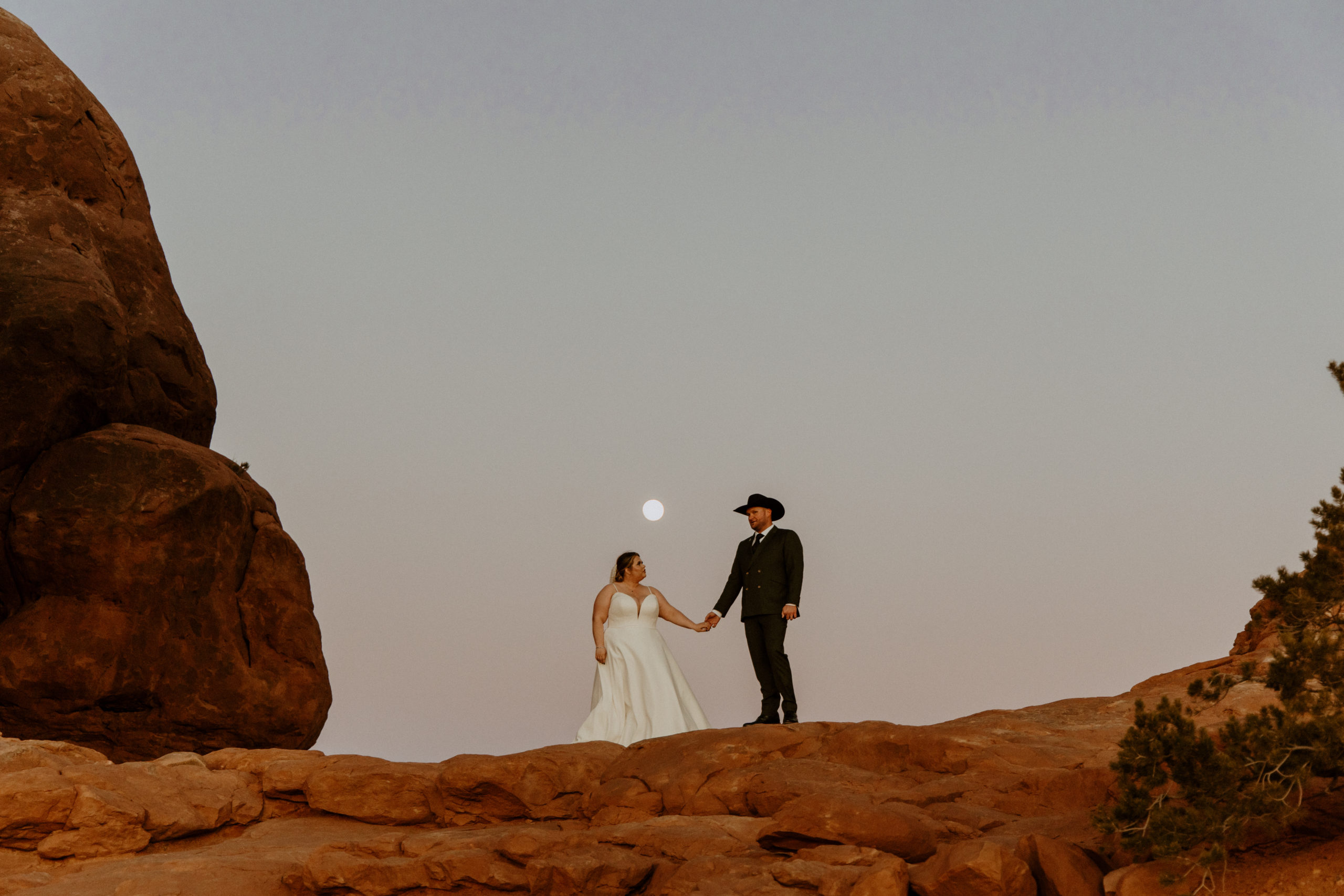 the couple standing by the moon as the sun sets