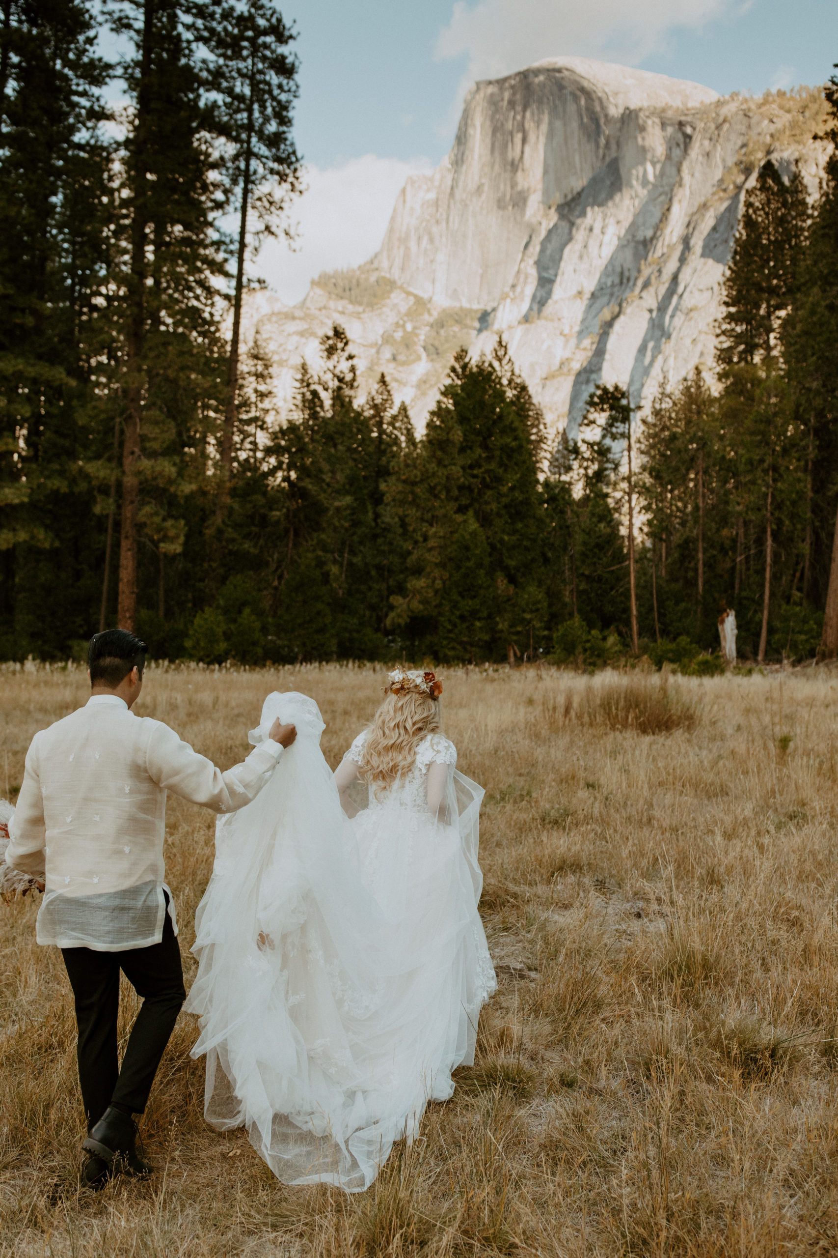 the groom holding the dress as the bride walks through their elopement in Yosemite 