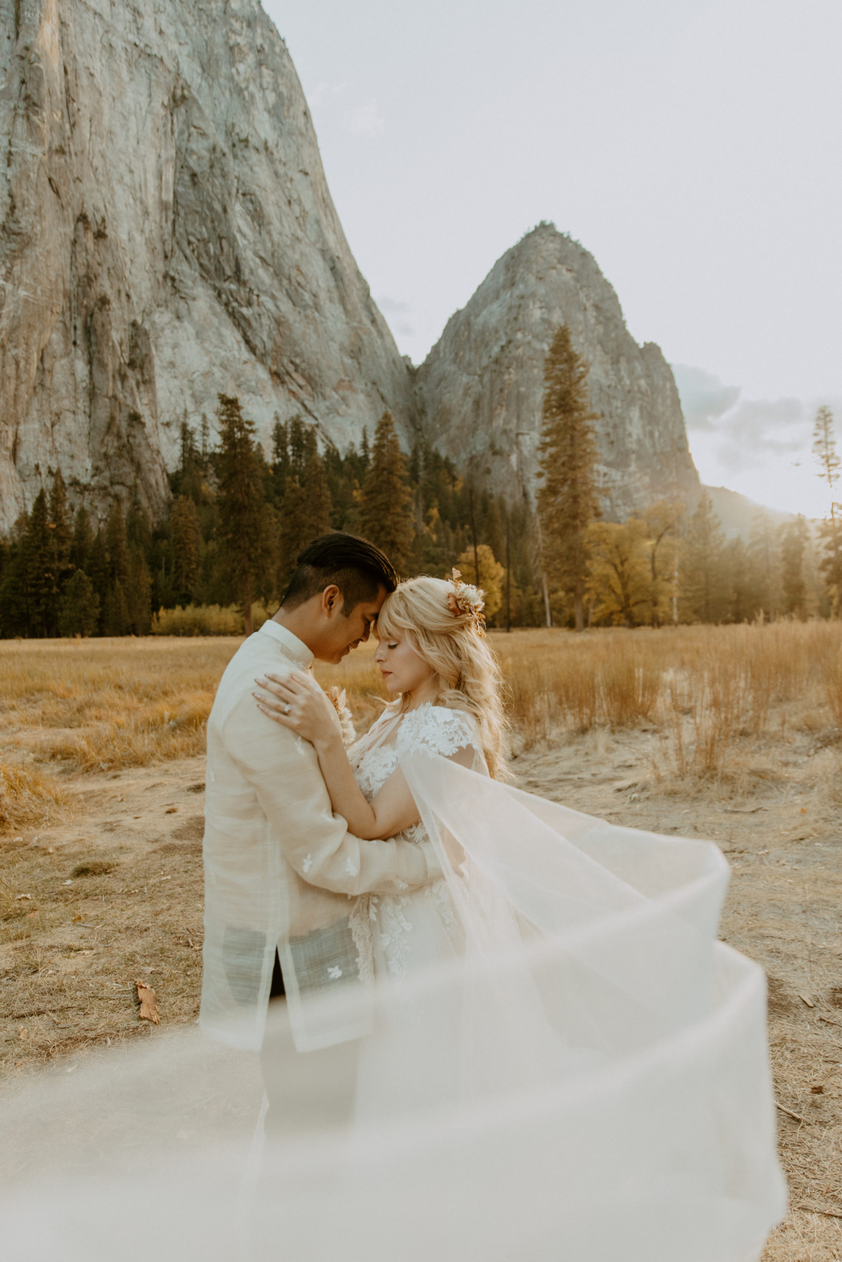 the couple touching foreheads with her veil blowing in the wind