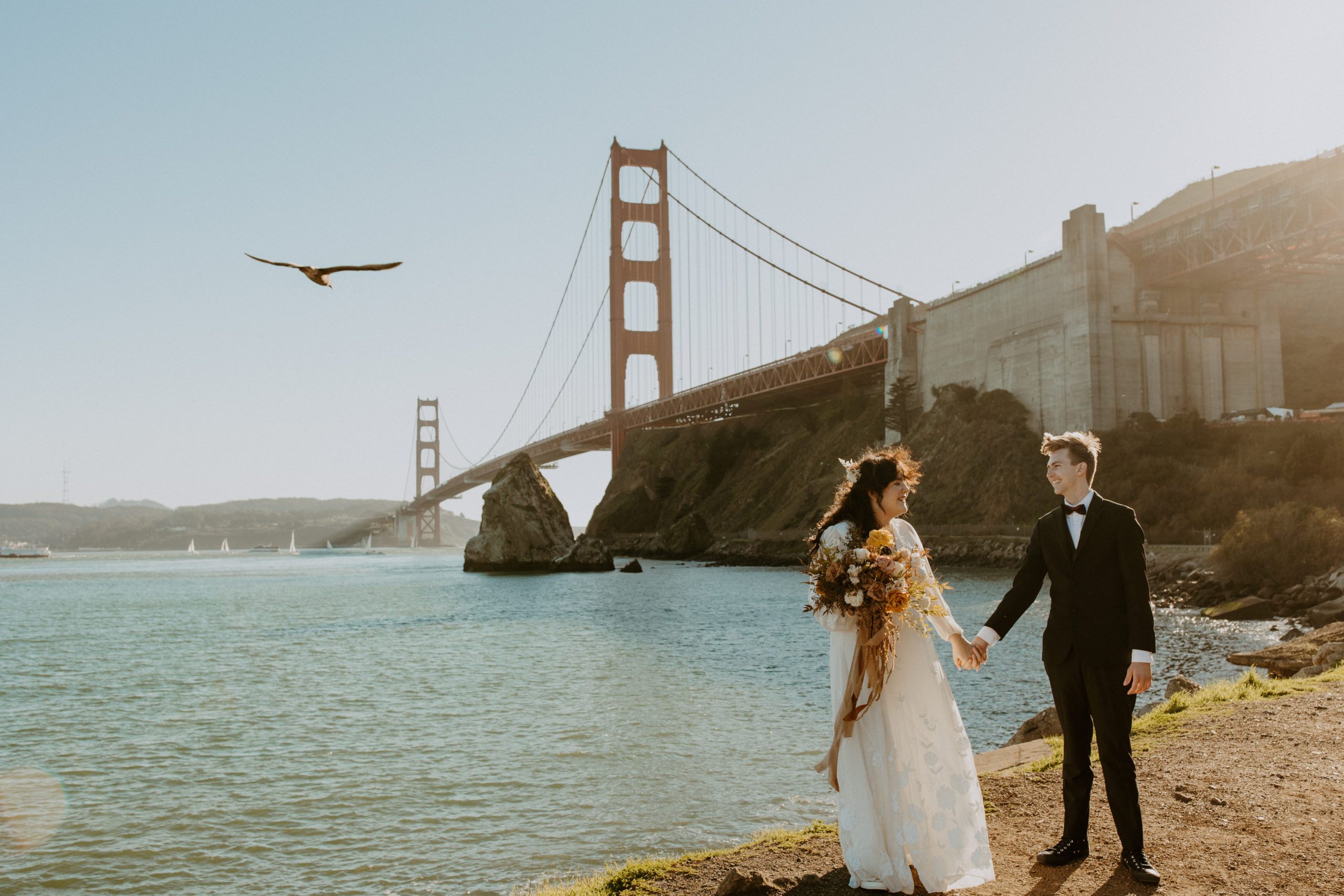 the couple standing on the shore near the Golden Gate Bridge
