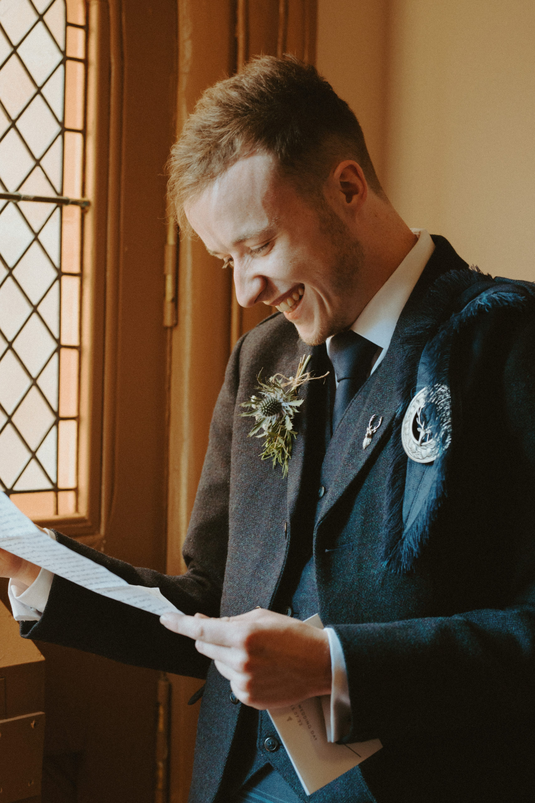 the groom smiling as he reads a letter