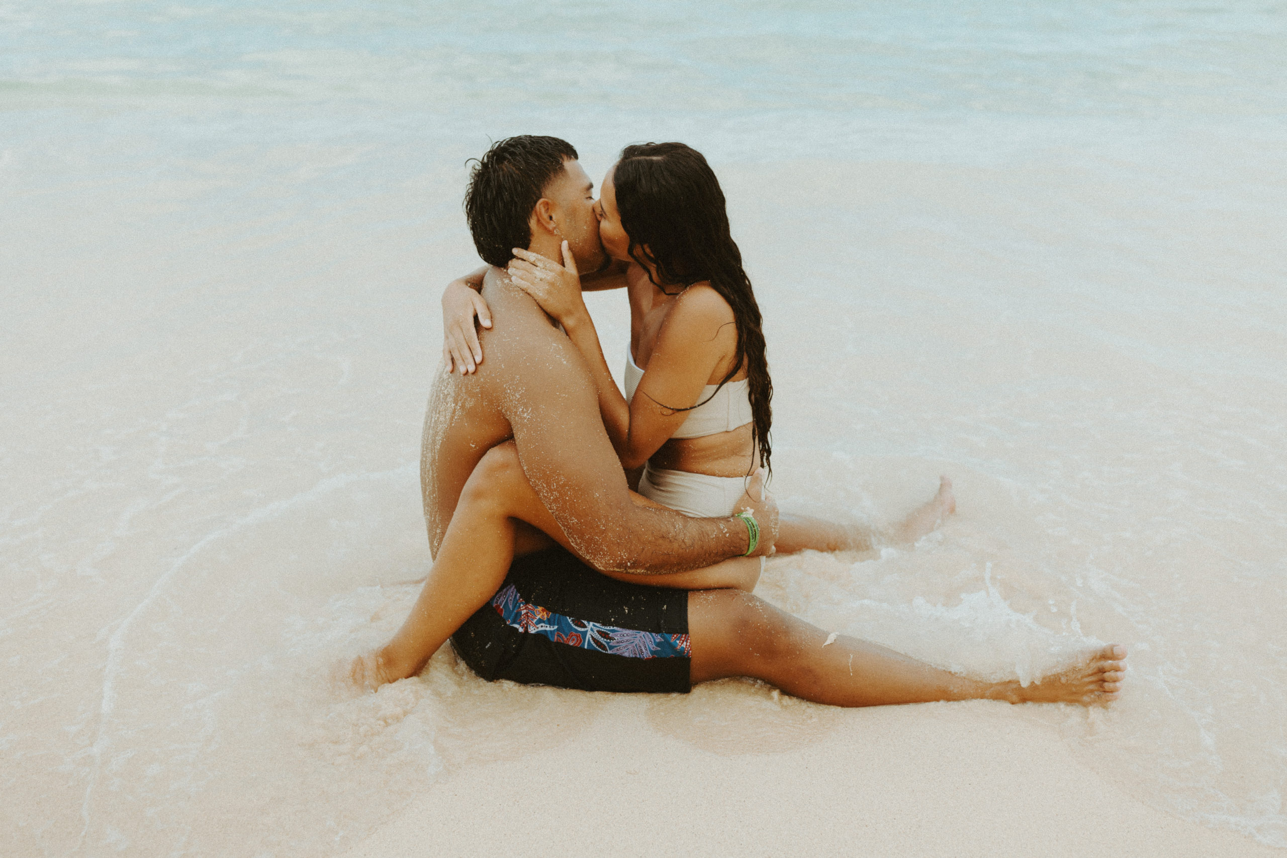 the couple kissing as they sit in the sand