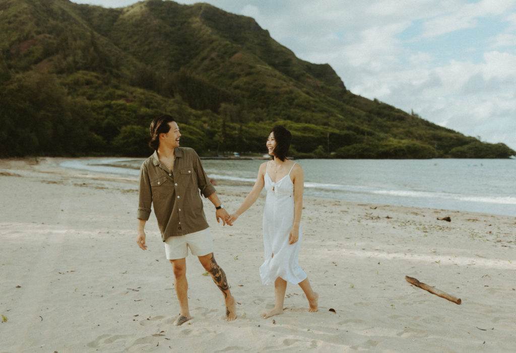 the couple holding hands on the beach as they walk towards the couples photographer