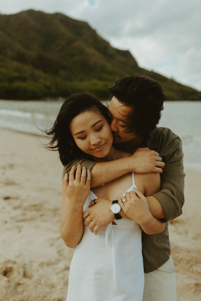 the fiance kissing her cheek on the beach in Hawaii for engagement pictures