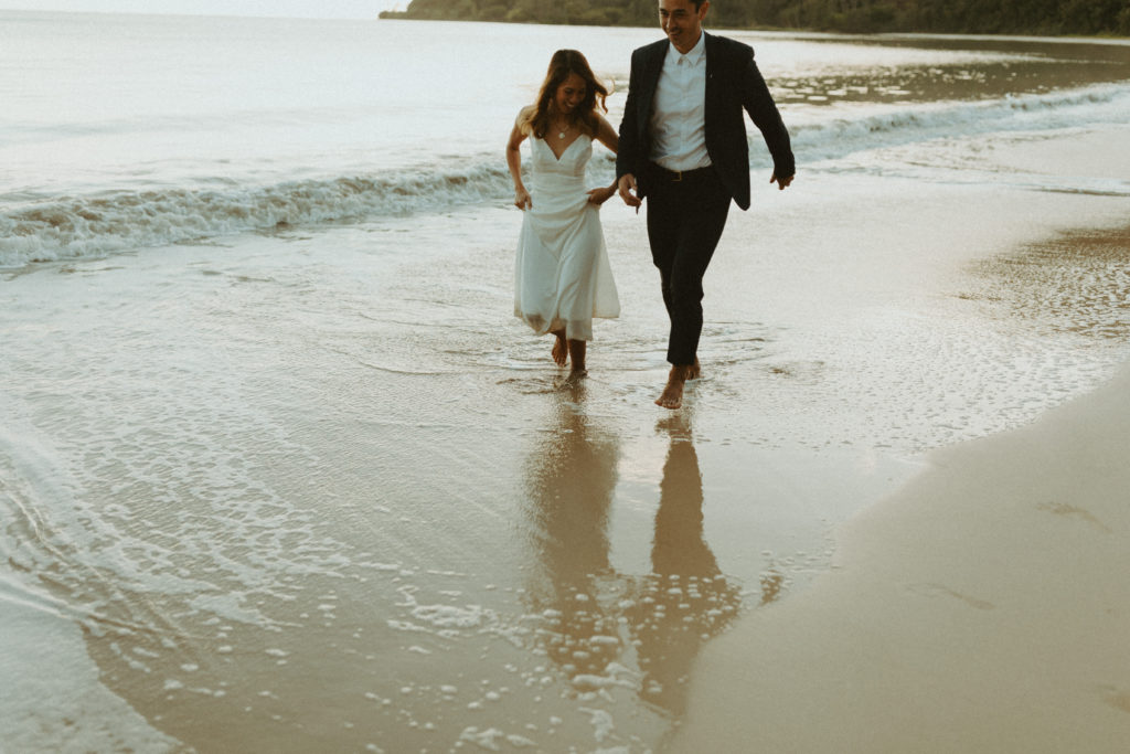the couple running through the water in their wedding dress and suit