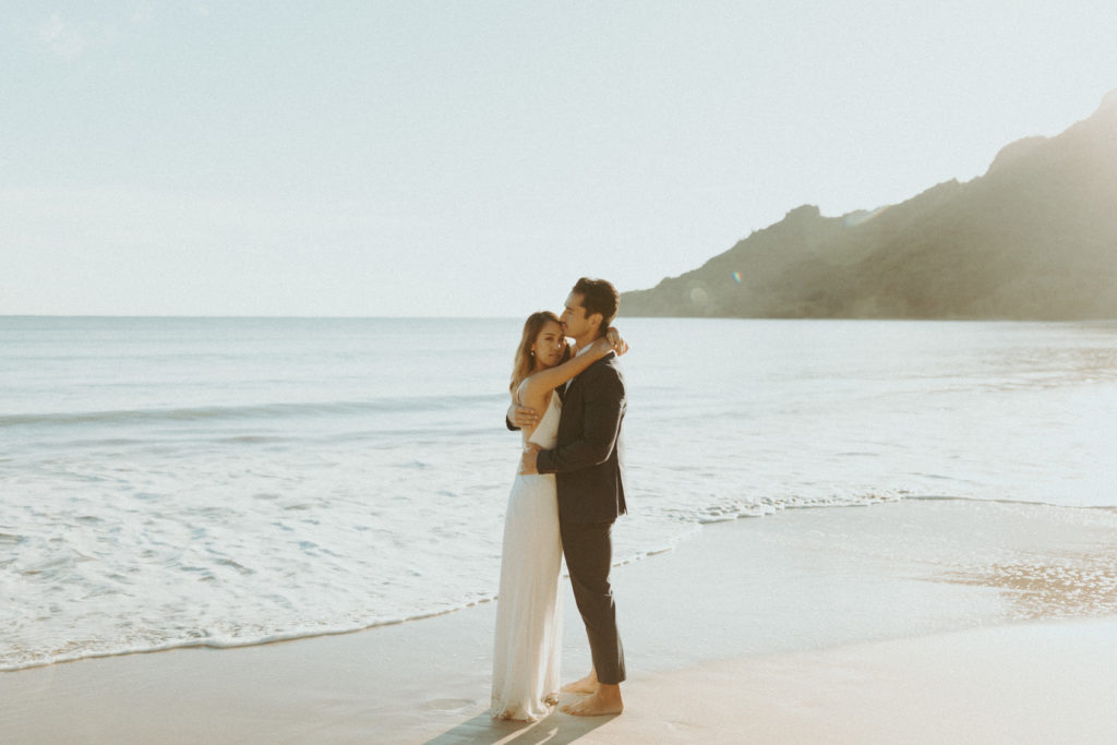 the couple hugging each other on the beach for the Hawaii photographer to capture