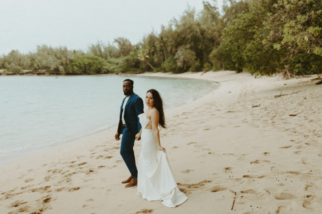 the wedding couple holding hands and walking down the beach