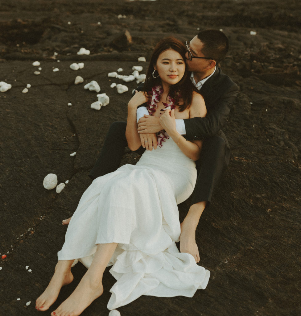 the groom kissing the bride's forehead as they sit on the lava rock