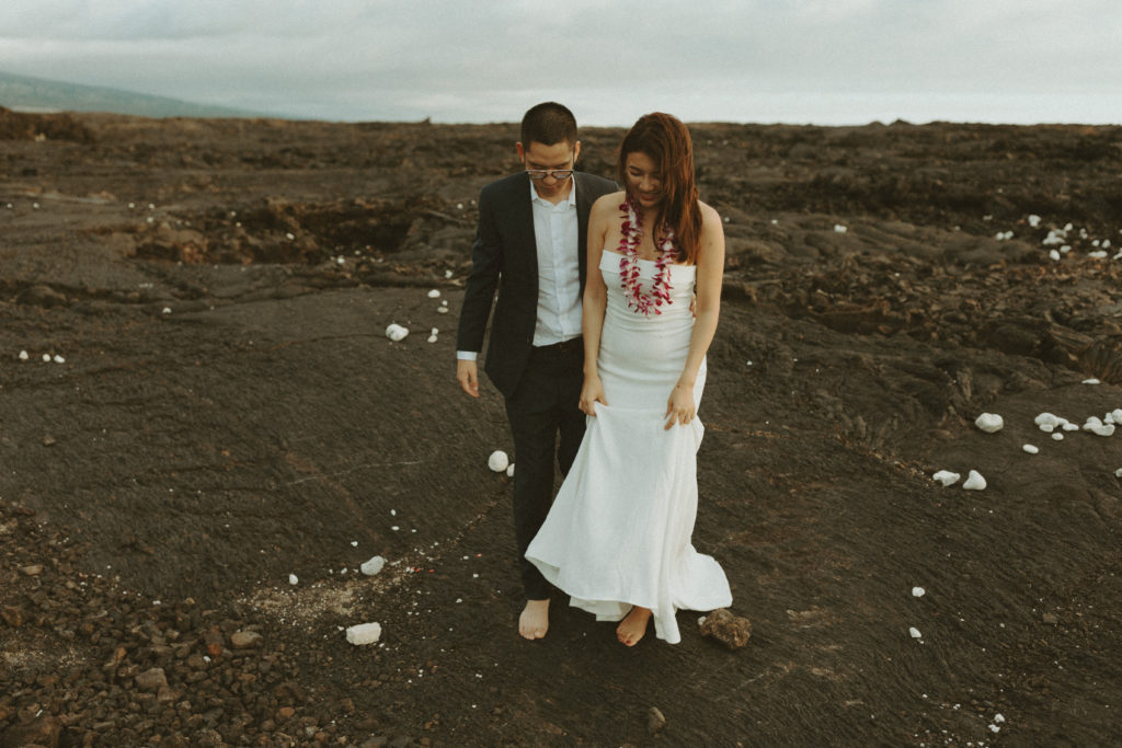 the bride and groom walking together in Hawaii on the lava rock