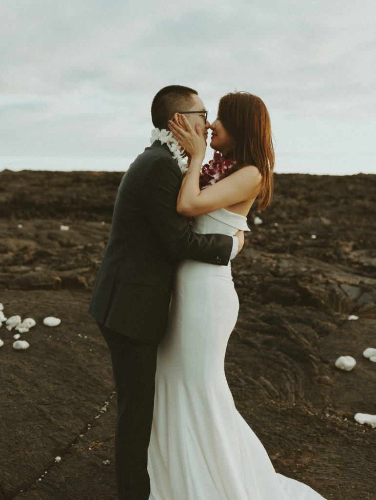 the wedding couple leaning in to kiss on the lava rock in Hawaii during their wedding