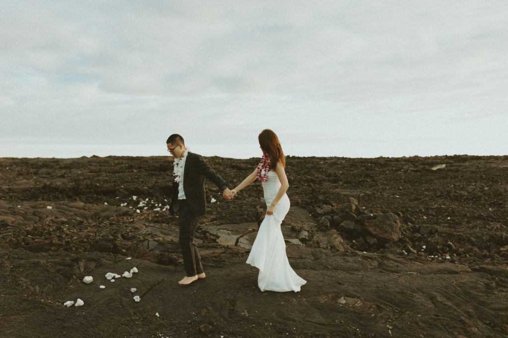 the couple walking along the lava rock as they hold hands for wedding photos
