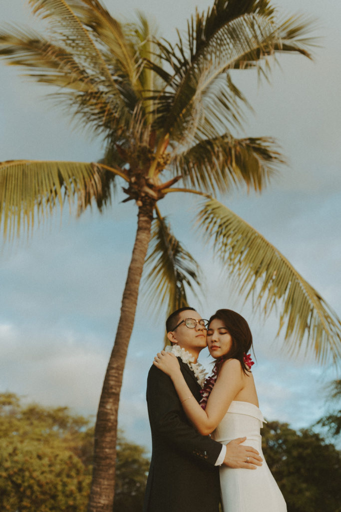the wedding couple posing together in Hawaii under the palm trees