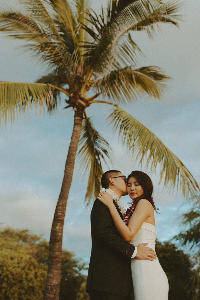 the wedding couple posing together underneath the palm trees