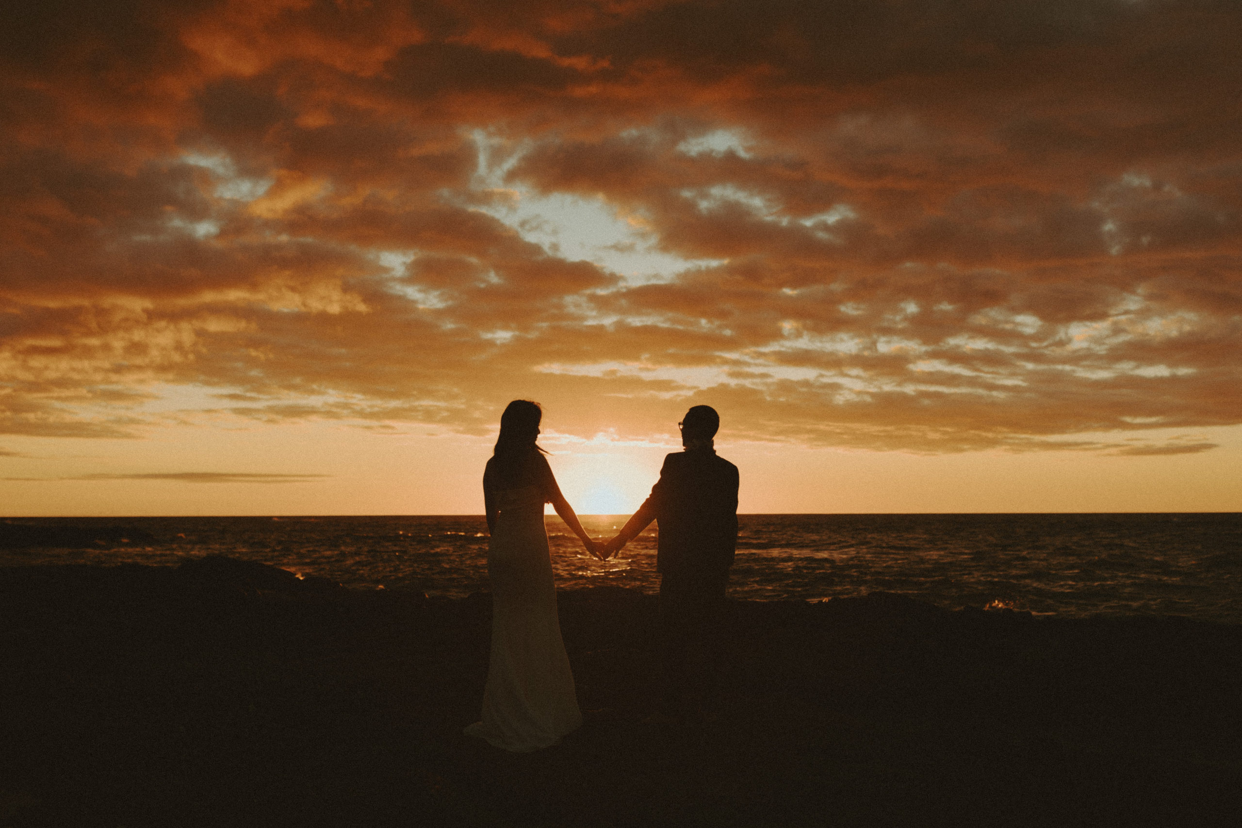 the wedding couple holding hands during the orange sunset in Hawaii