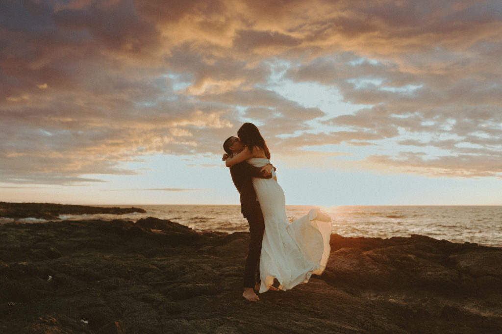 the groom lifting up the bride for sunset pictures during their Hawaii wedding