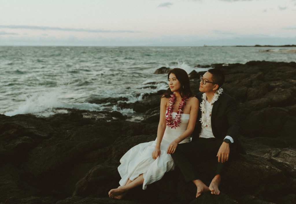 the bride and groom sitting on lava rock in Hawaii during their Big Island Kona wedding