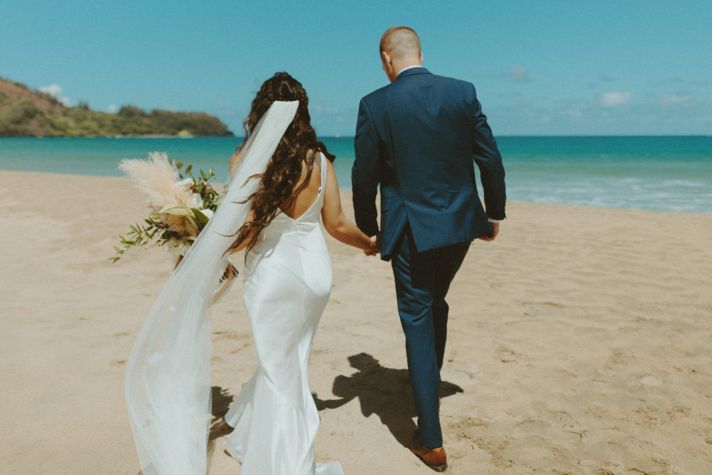 the couple holding hands and walking down the beach during their Kauai elopement