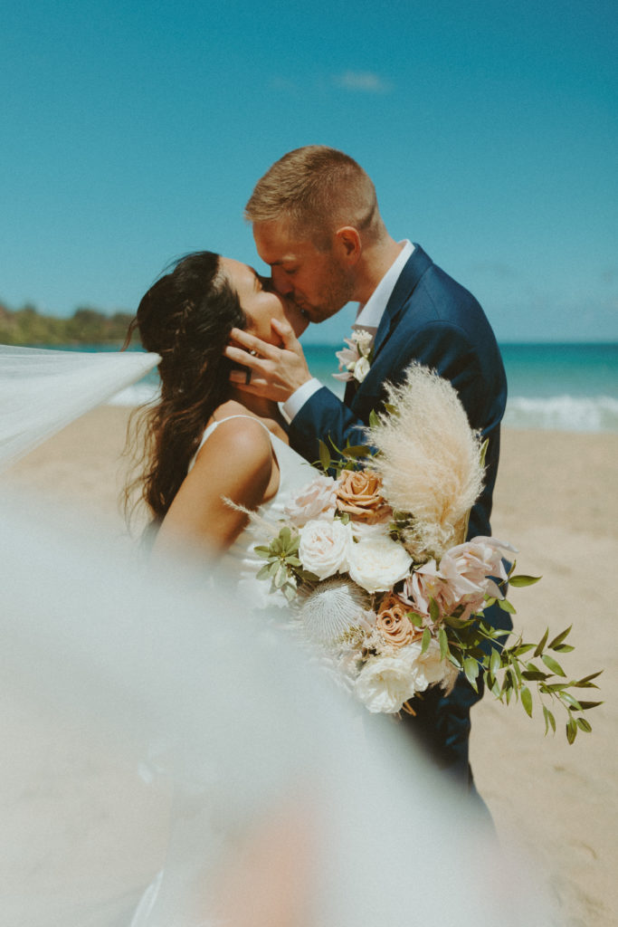 the couple kissing on the beach with the veil blowing in the wind 