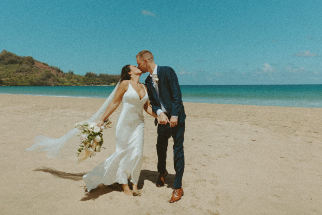 the couple kissing as they walk down the beach together in Hawaii