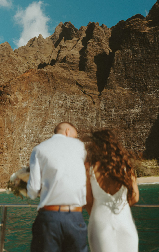the couple leaning on the edge of the boat in Hawaii during their Kauai elopement