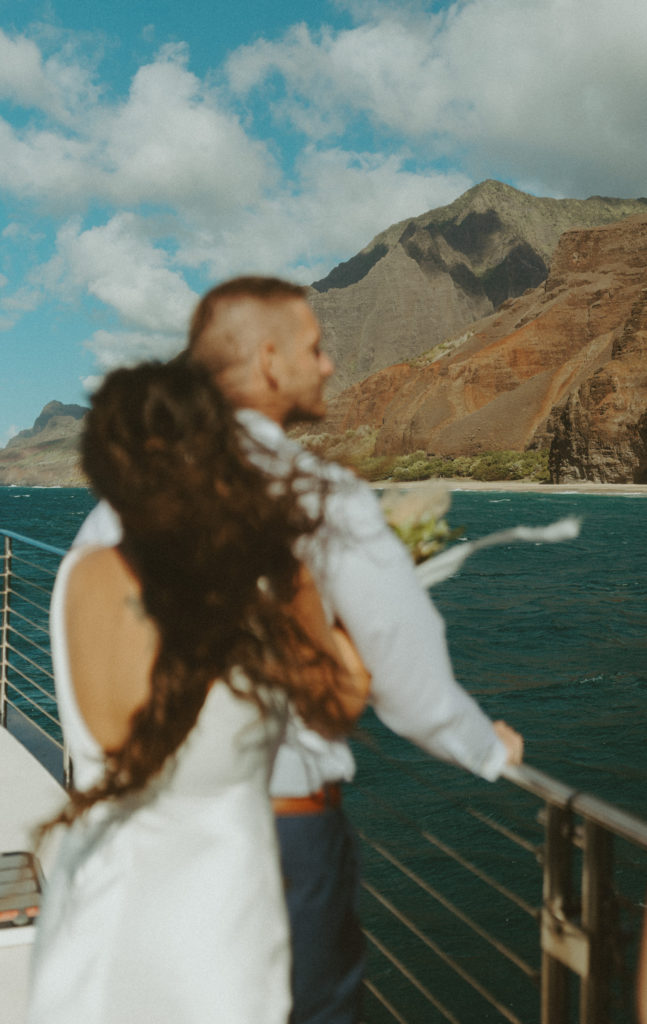 the bride wrapping her arms around the groom as the ride on the boat in Hawaii