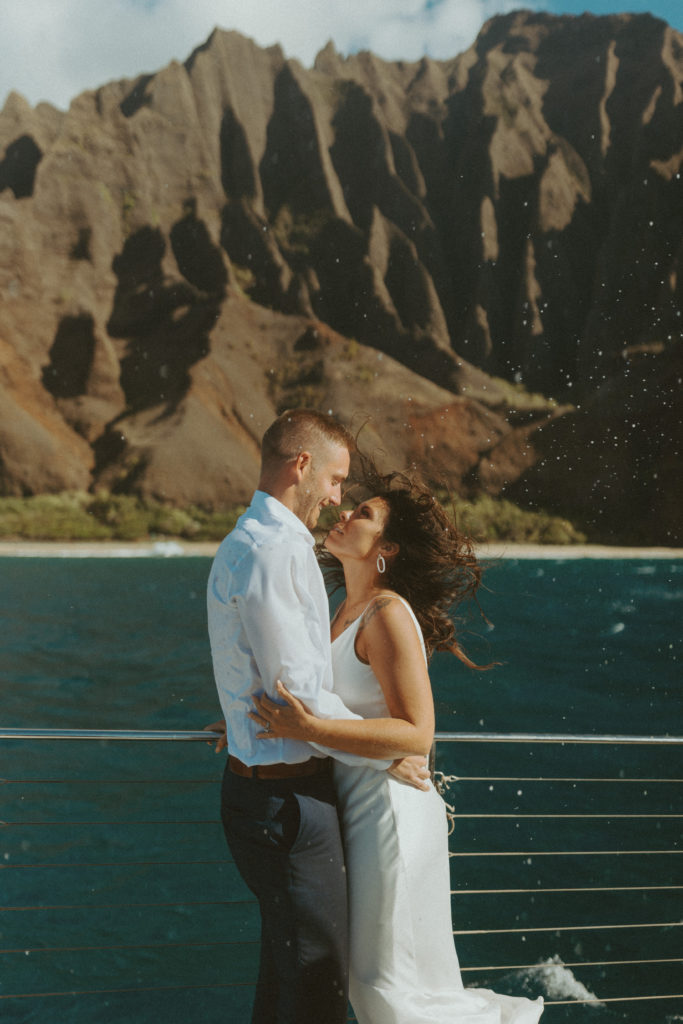 the wedding couple wrapping their arms around each other as their hair blows in the wind on the boat