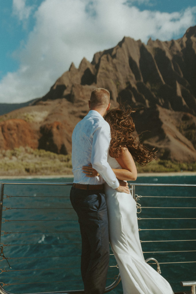 the wedding couple hugging one another as they look out over the ocean 