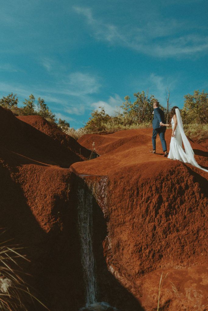 the elopement couple holding hands and walking along the canyon in Hawaii