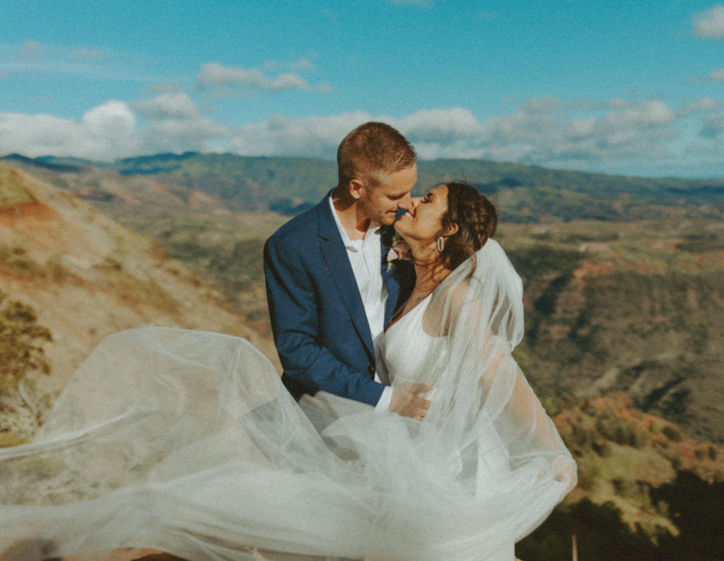 the couple kissing at the top of the canyon as the wedding veil blows in the wind
