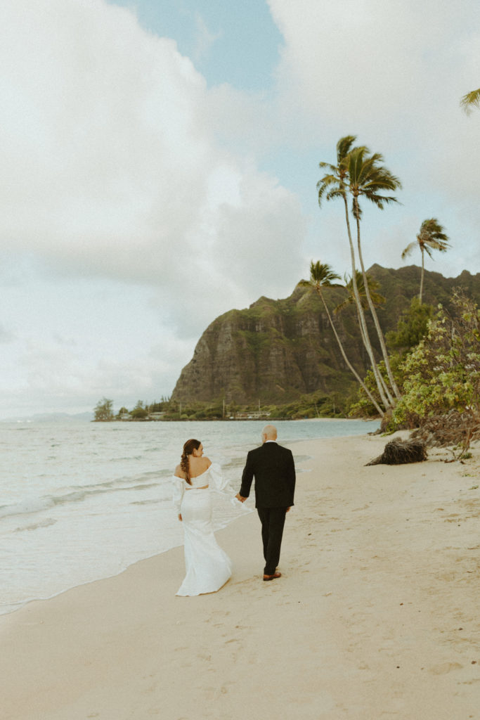 the wedding couple walking down the beach together in Oahu as they hold hands