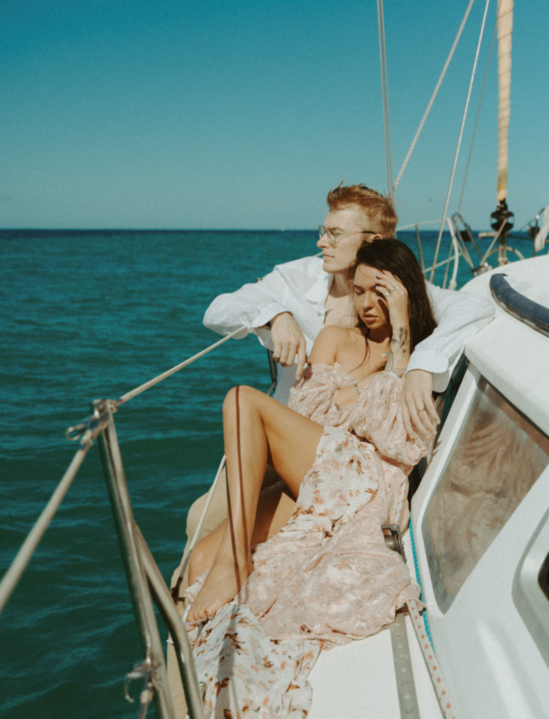 the couple sitting on the side of the sailboat in the Oahu sun
