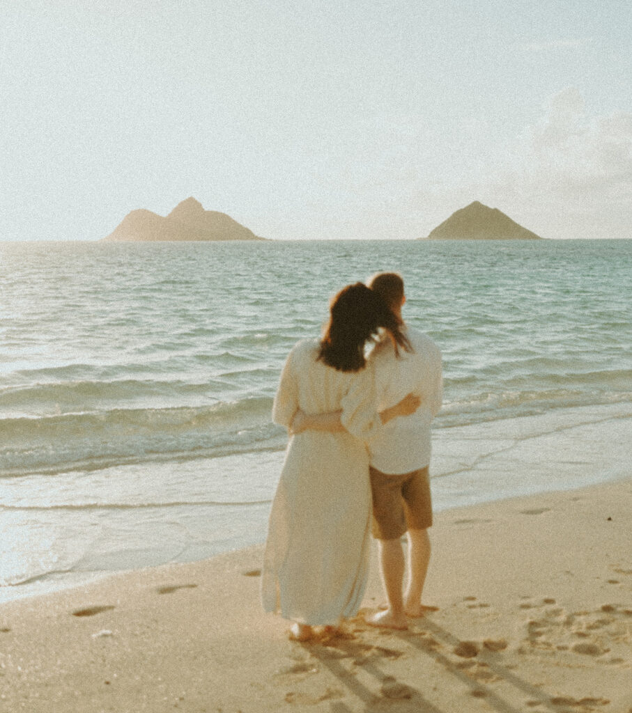 A couples photos on the beach in oahu posing in the sand and playing in the ocean
