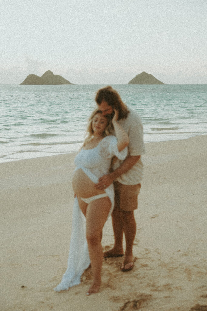 a maternity photoshoot in oahu hawaii with a couple playing on the beach and in the ocean

