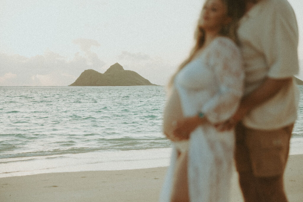 a carefree couple posing for a maternity session on a beach in oahu