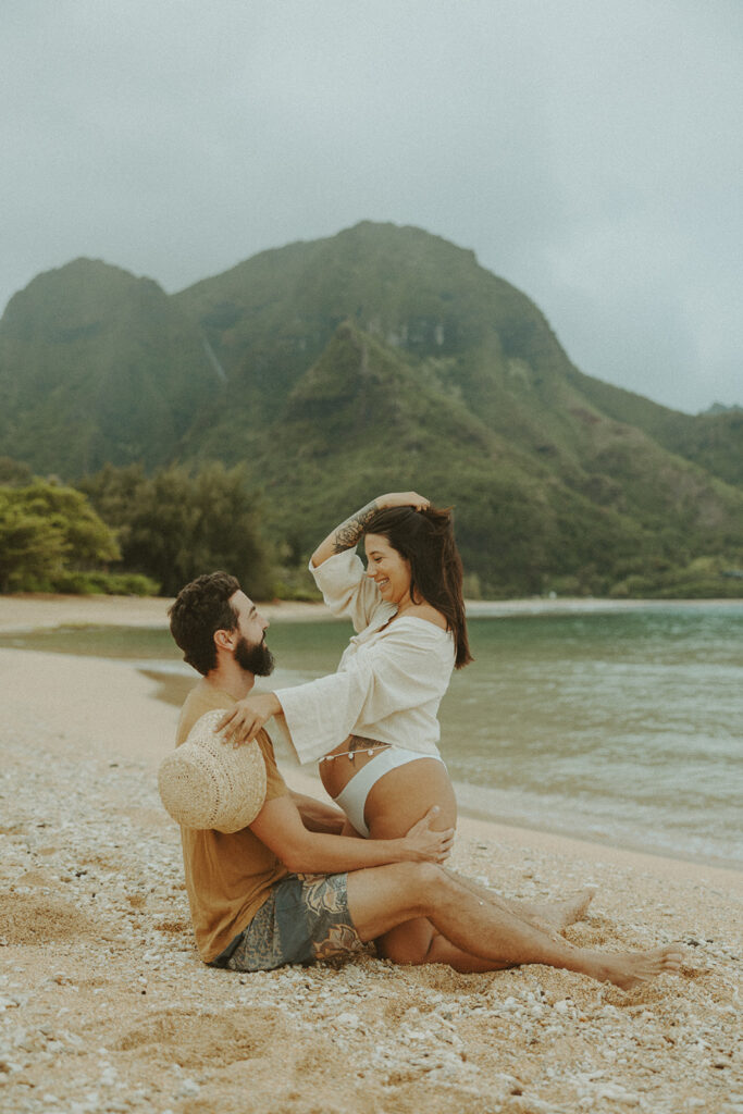 a couples posing on a beach in kauai for their maternity photoshoot
