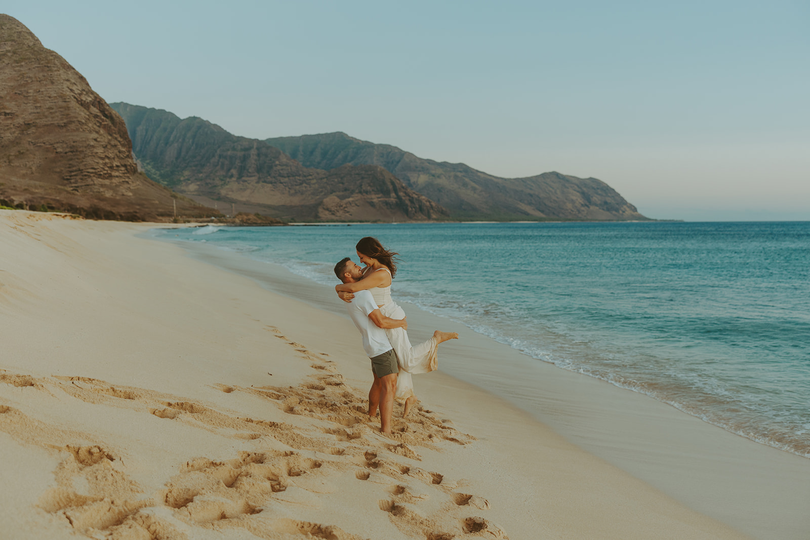 A dreamy beachside engagement session in Hawaii, with stunning mountains in the background.