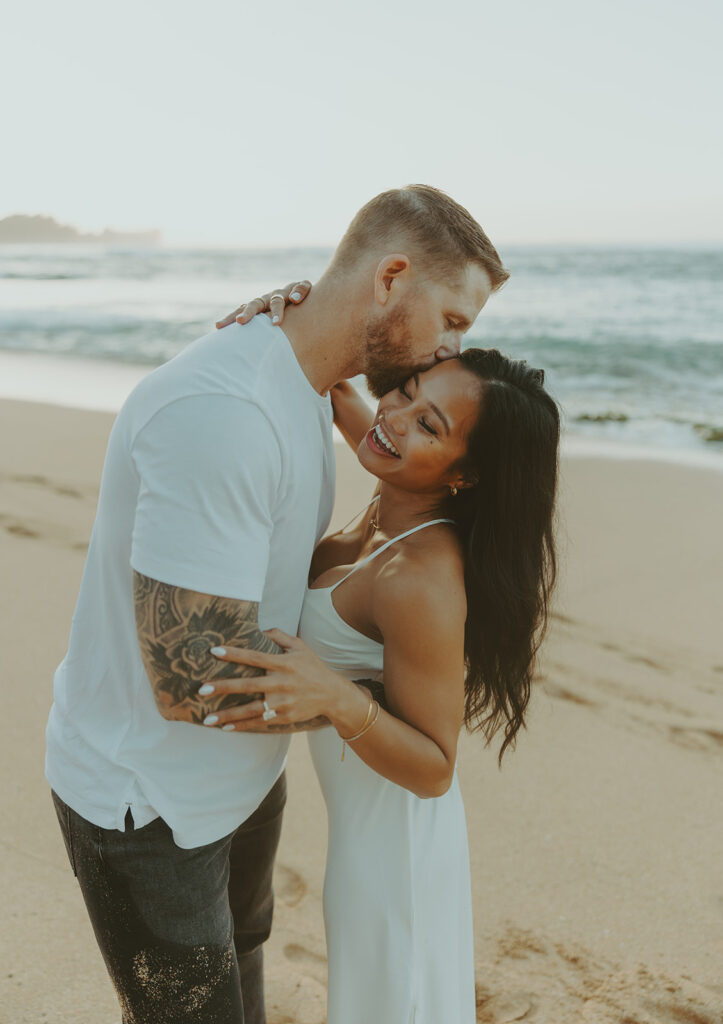 Engaged couple hugging and laughing during beach photoshoot
