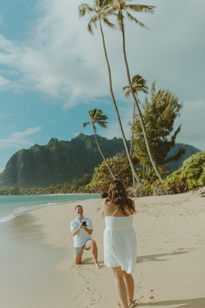 Nicholas down on one knee proposing to Nicole on a beach in Hawaii.
