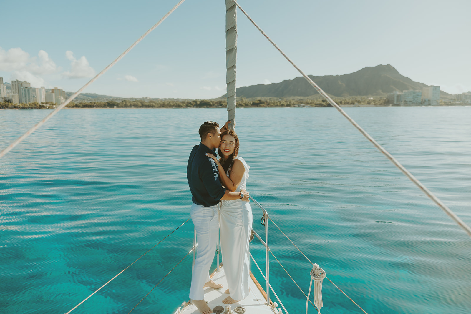 Romantic couple embracing on a sailboat during a Waikiki sailboat photoshoot in Oahu, Hawaii