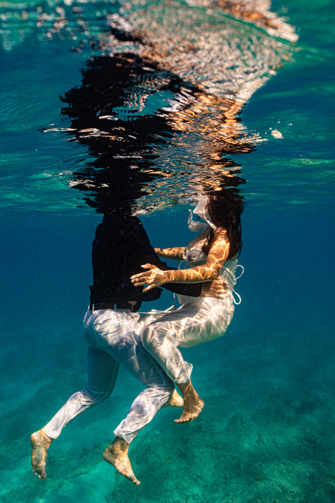 Underwater photo of couple swimming hand-in-hand after their Oahu sailboat shoot