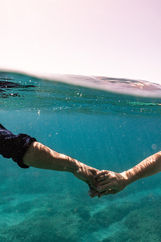 Underwater photo of couple swimming hand-in-hand after their Oahu sailboat shoot