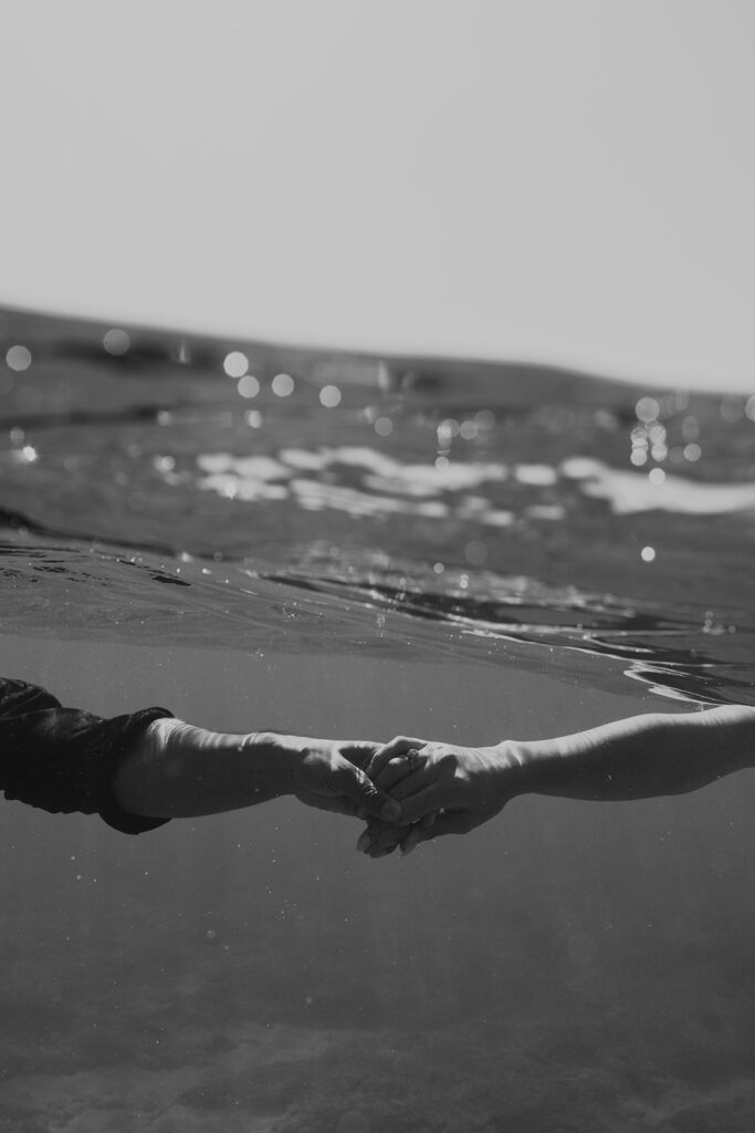 Underwater photo of couple swimming hand-in-hand after their Oahu sailboat shoot
