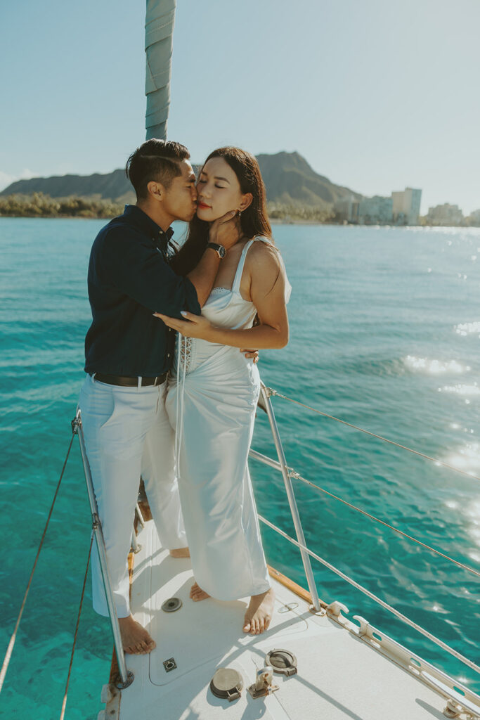 Romantic couple embracing on a sailboat during a Waikiki sailboat photoshoot in Oahu, Hawaii
