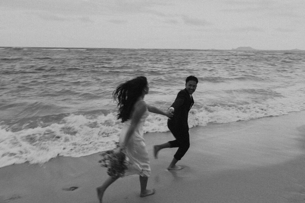 Bride and groom walking barefoot along Kaaawa Beach during golden hour
