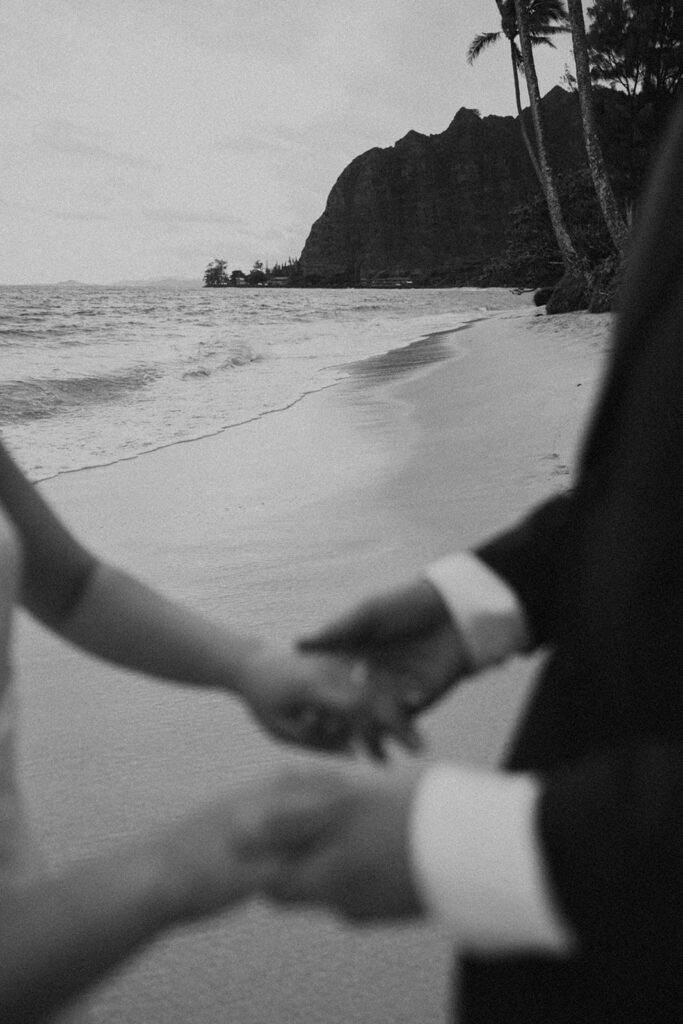 Bride and groom walking barefoot along Kaaawa Beach during golden hour
