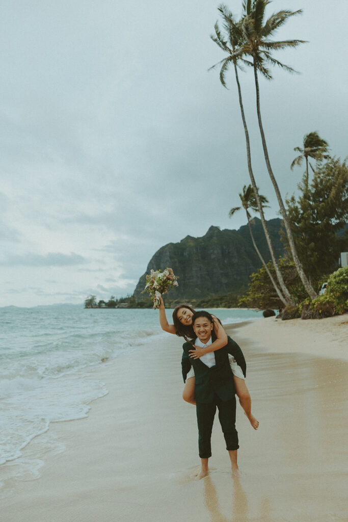 Bride and groom walking barefoot along Kaaawa Beach during golden hour
